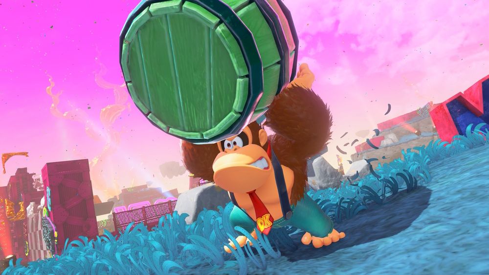 Screenshot from Donkey Kong Bananza. Donkey Kong carrying a barrel above his head looking grumpy as hell. He’s wearing his signature tie but also some jeans and suspenders. 