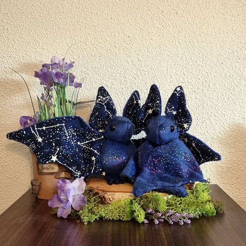 Deux peluches de chauve-souris, bleu foncé avec des paillettes multicolores, et un tissu constellations à l'intérieur des ailes et des oreilles 