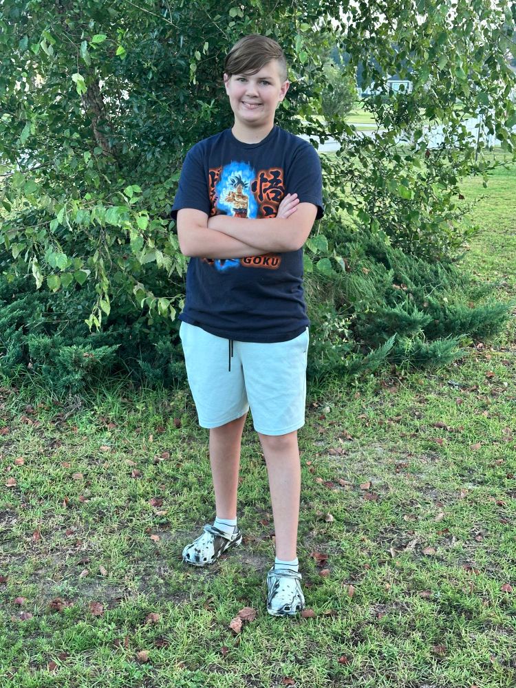 A young man in a Dragonball t-shirt indulges his father by posing in front of a tree for an obligatory First Day of School picture. 