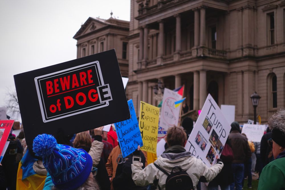 Protesters at a rally in Lansing MI, 5th April 2025. Sign in foreground reads “Beware of DOGE”