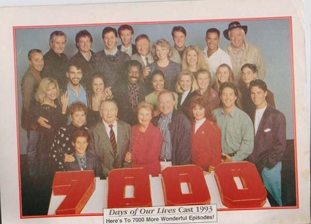 Sideways promotional photo of the Days of Our Lives cast from 1993, commemorating the show’s 7000th episode. Dozens of cast members are arranged in rows, dressed in early ’90s fashion—blazers, shoulder pads, and bold prints. The red vertical text reads “7000,” and the caption says “Here’s to 7000 More Wonderful Episodes!” The tone is celebratory and communal, capturing a milestone moment in daytime television history.

