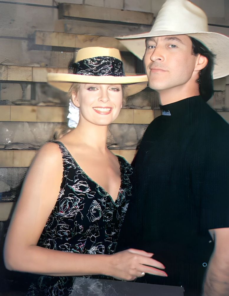 Behind-the-scenes photo of Deidre Hall and Drake Hogestyn in Mexico, 1991, during the filming of the Chichenitza storyline for Days of Our Lives. Dee wears a floral dress and wide-brimmed hat, while Drake is dressed in black with a matching hat. They stand close together in front of a stone wall, relaxed and smiling. Though their characters were scripted to drift apart, this candid moment captures the offscreen ease and chemistry that fans never stopped rooting for.