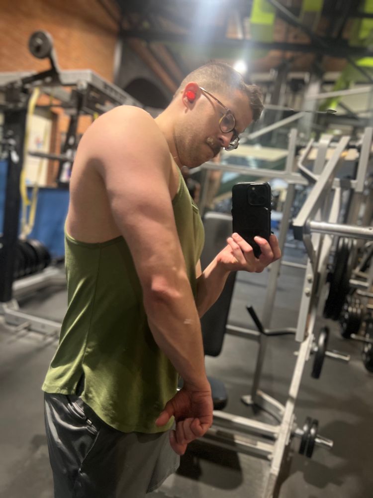 Gym mirror selfie of OP flexing tricep with prominent vein in forearm