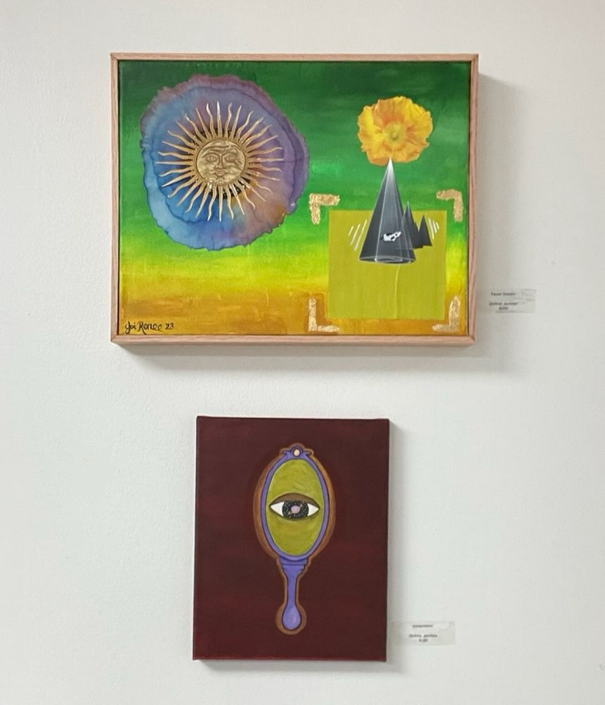 Joi’s art hanging on a gallery wall. The top piece is a multicolored mixed media abstract painting and the bottom is an acrylic and watercolor painting of a hand mirror with an eye in the middle with the universe as their iris and planet as the pupil 