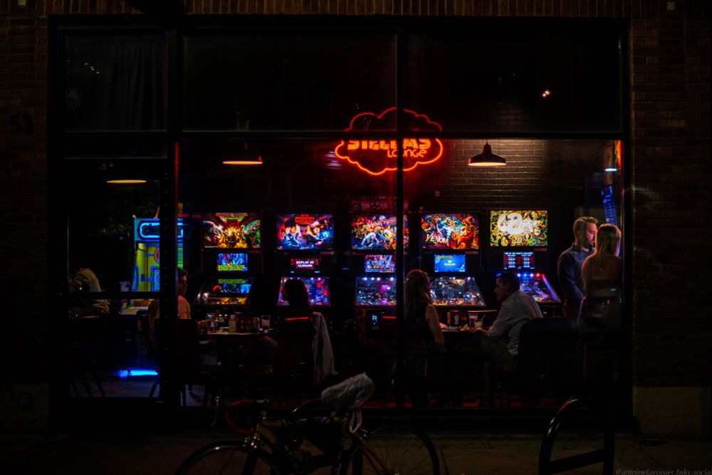 Night scene, looking into an arcade tavern filled with merry pinball machines and carnival games. Three male/female couples are seated, silhouetted by the pinball lights XH1 TTArtisan 35mm f1.4 0049 hrs 3200 iso 1/125 processed in dx0 pureraw