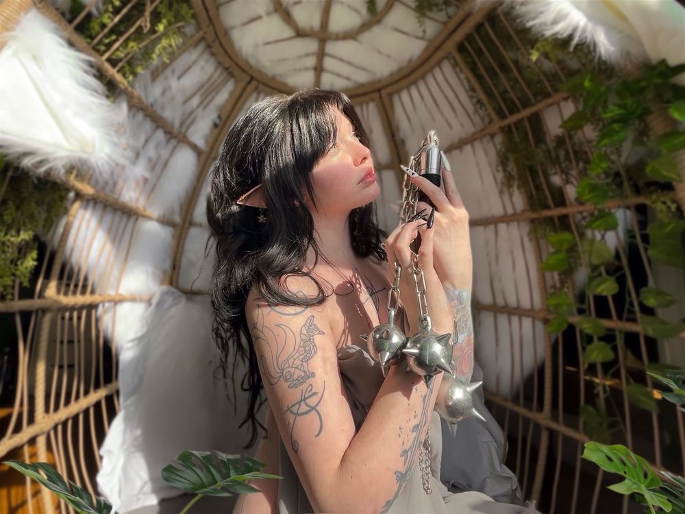 An elfen person either green eyes and black hair holds a flail while looking off into the sun