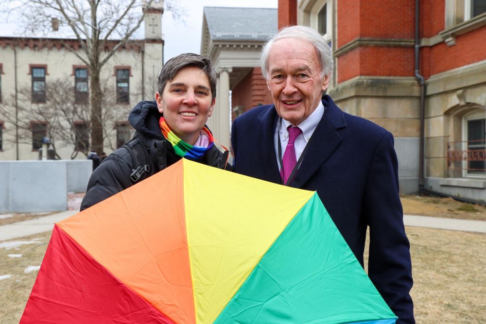 Senator Markey and a rally participant smile and hold a rainbow umbrella.