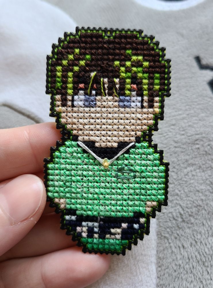 a small cross stitch character with green and brown hair, a green sweater, and green boots