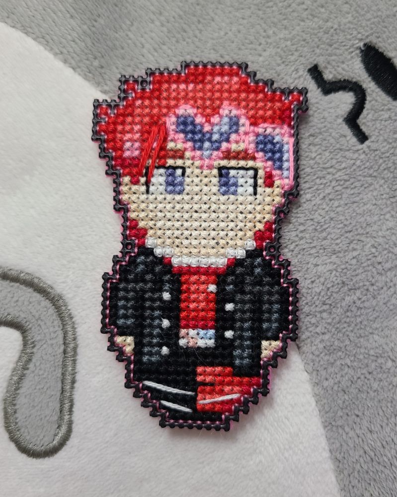 a small cross stitch character with red hair, pink heart goggles, and black and red clothes.