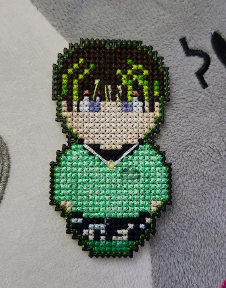 a small cross stitch character with green and brown hair, a green sweater, and green boots