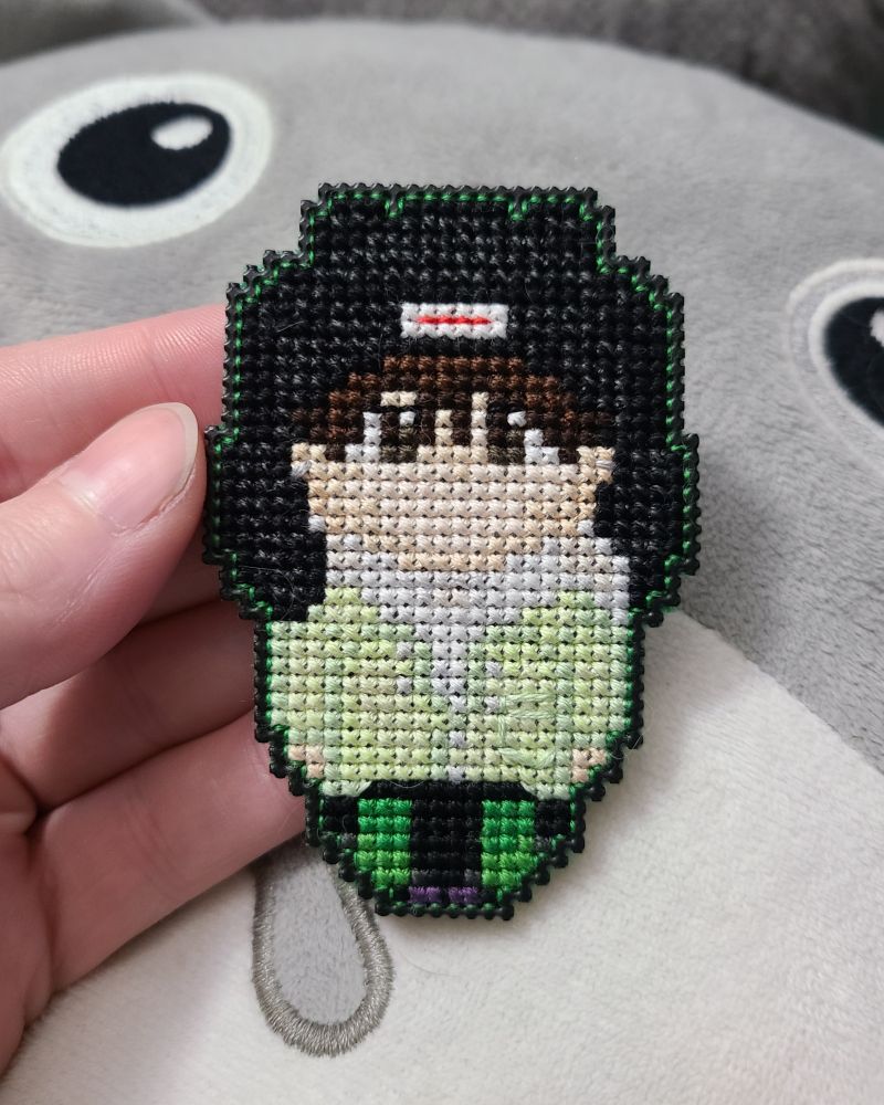 a small cross stitch character with a black hat, green cost, and black and green pants