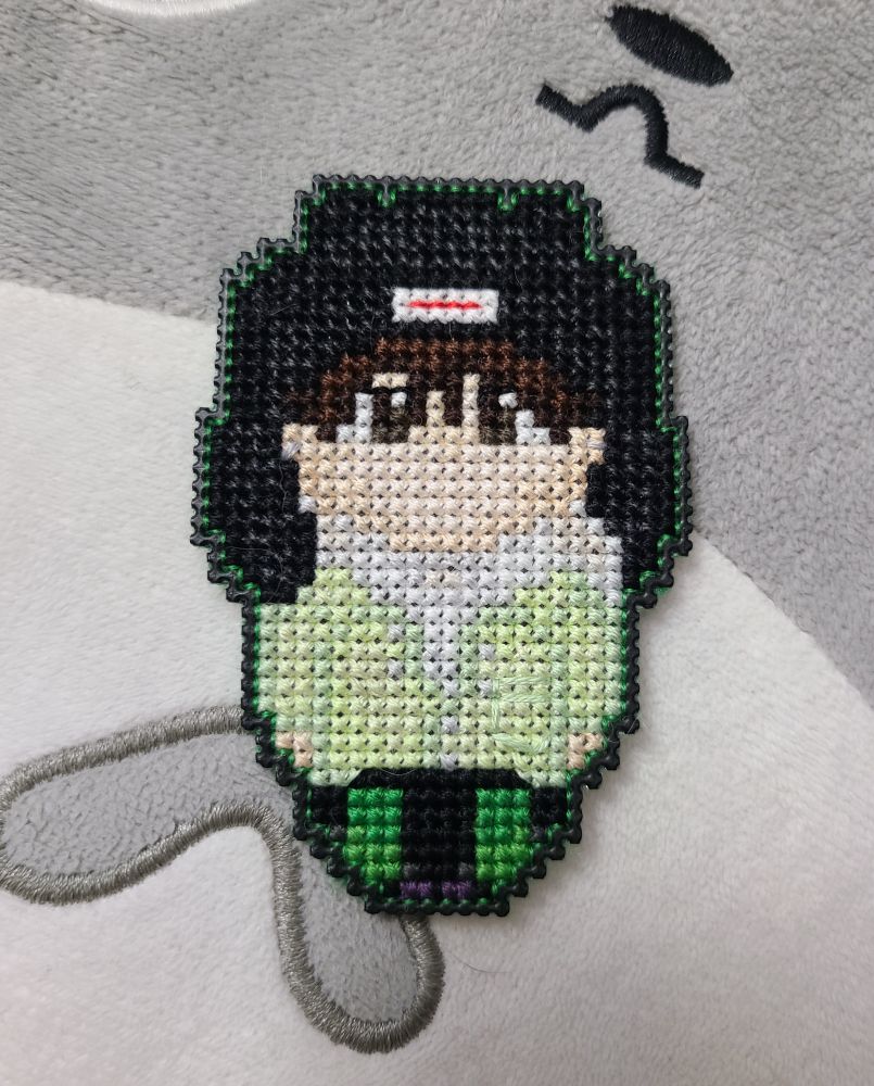a small cross stitch character with a black hat, green cost, and black and green pants