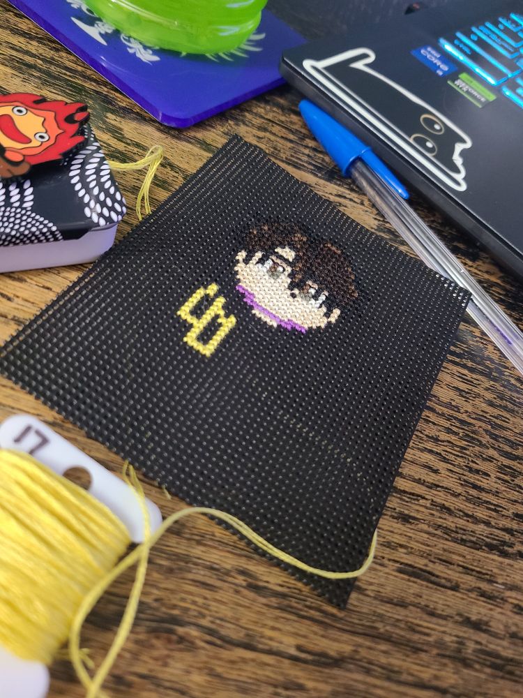 a WIP cross stitch of a character with brown hair and a yellow jacket