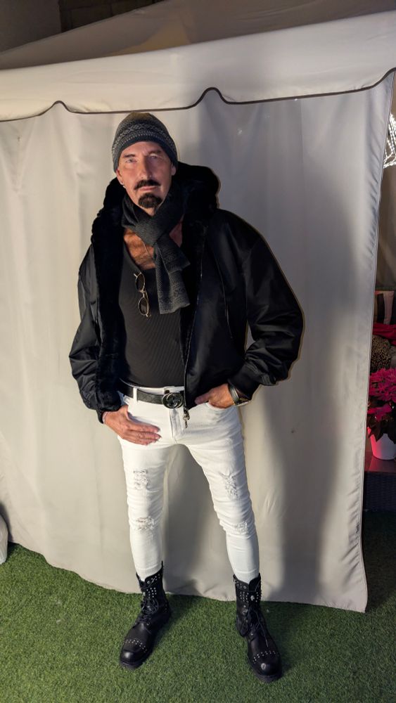 Alex dressed for the chill. Warm hat, warm black coat, scarf over vest. White ripped jeans with a dark belt and designer bovver boots. 