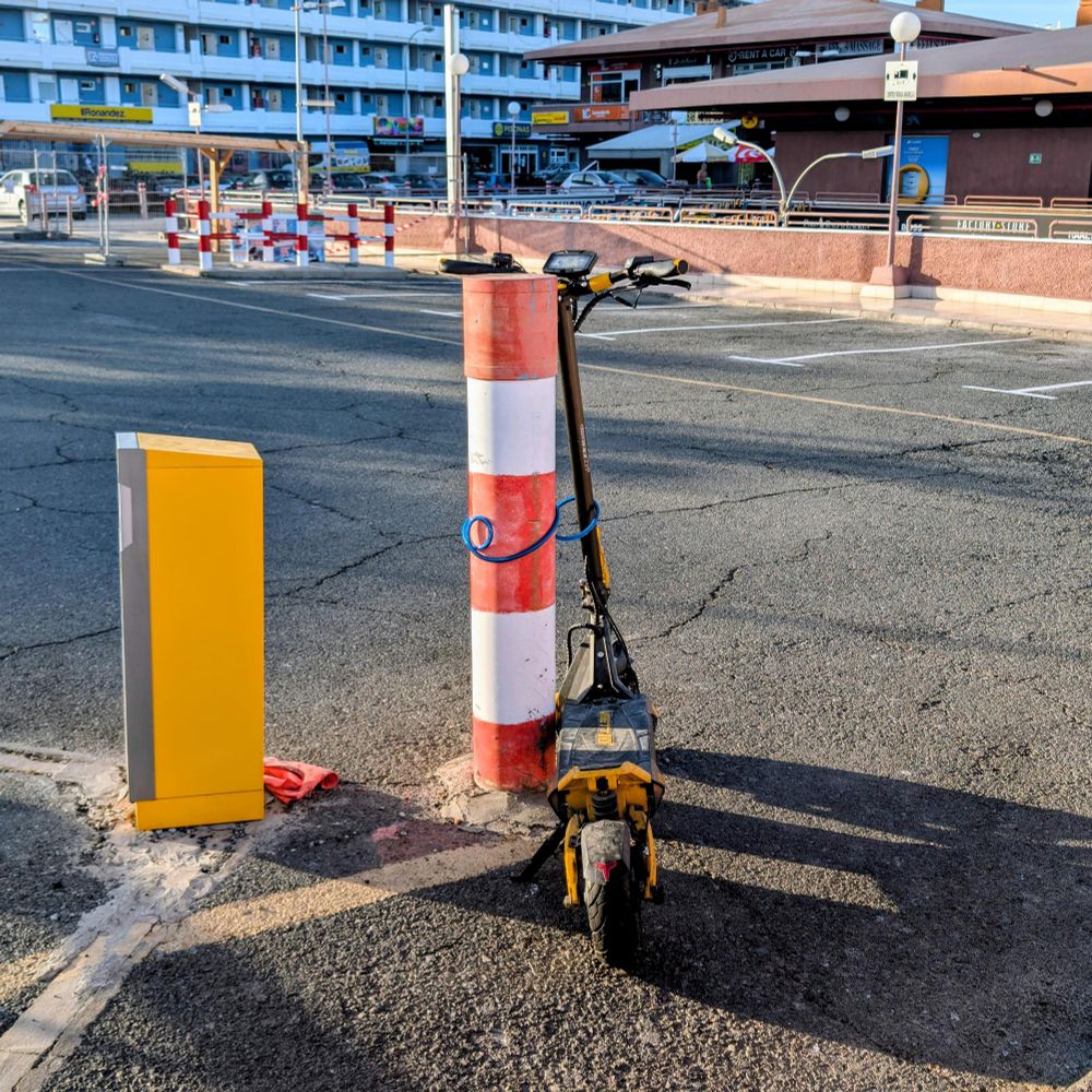 An e-scooter chained to a bollard. Just the handlebars to a bollard. Nothing stopping the chain being lifted off the bollard. 