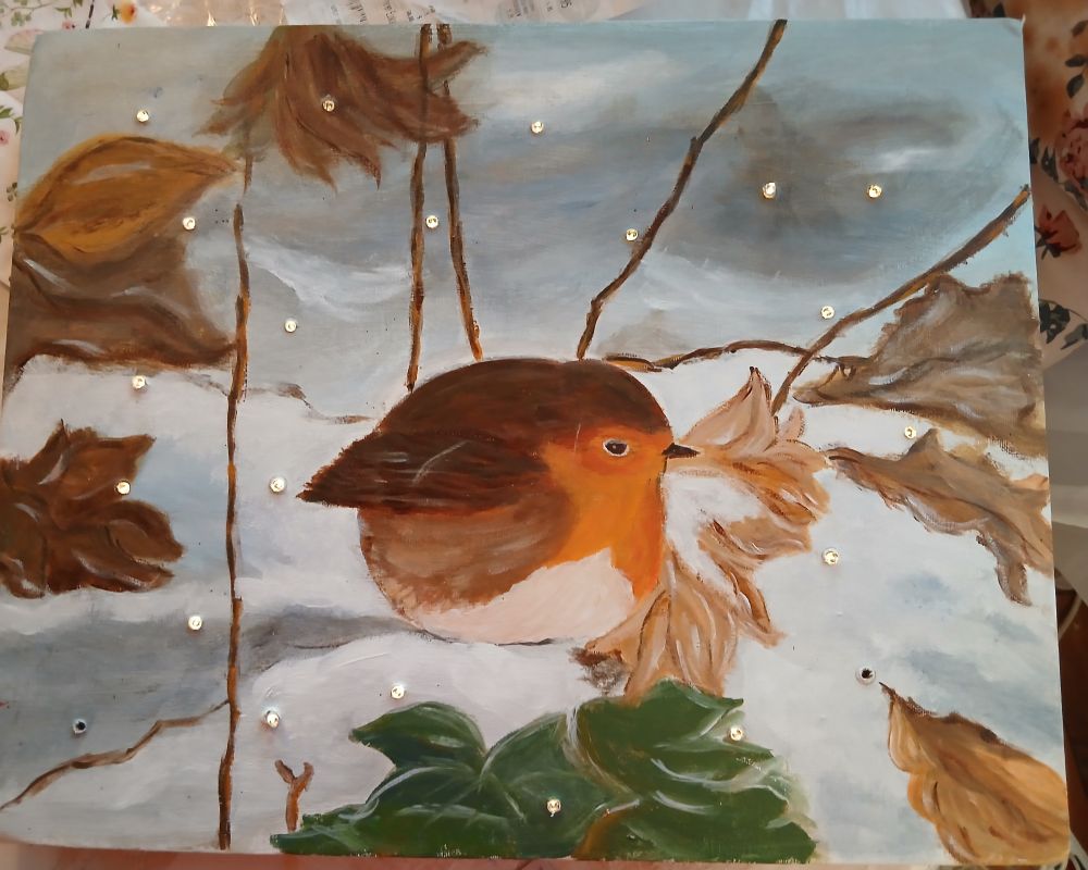 Gemaltes Bild eine Rotkehlchens mit braunen Blättern. Blauweisser Hintergrund. Lämpchen 