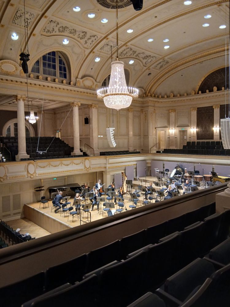 Konzertsaal mit Kronleuchtern, Musiker*innen im Orchestergraben 