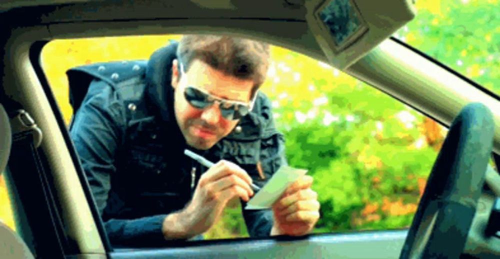 a man wearing sunglasses is writing on a piece of paper in his car