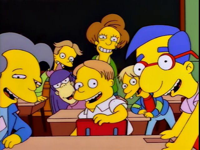 A screencap from The Simpsons. Students and a teacher look at the camera, waiting for Bart to “say the line”