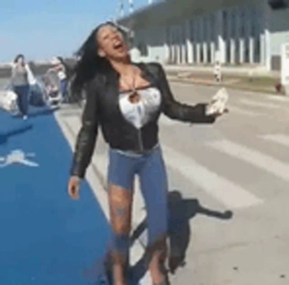 a woman in a leather jacket and shorts is standing on a sidewalk holding something in her hand .