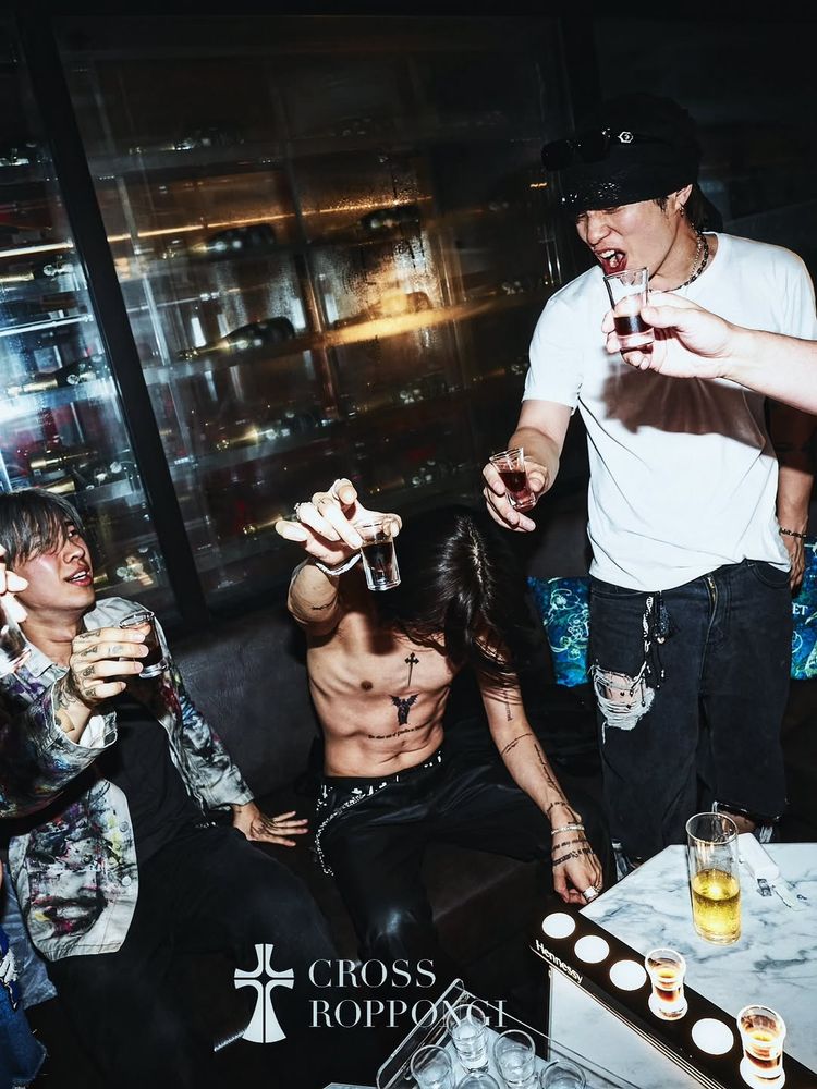a picture from the same club. This time Yijeong is sitting down on a black couch. He's holding up a shot glass and his head is tilted down so his hair is obscuring his face. He is also still very shirtless. There are other vendors members on either side of him, and everyone is holding up a shot glass in a toast. 