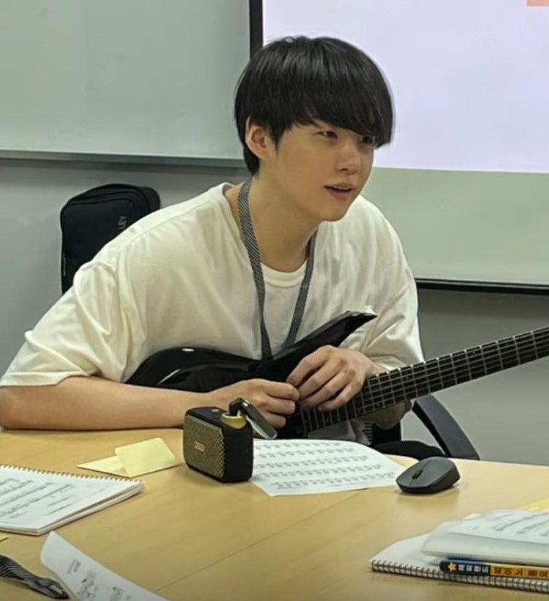 yoongi looking very soft with a white shirt, no make up, loose black hair and a guitar on his arms