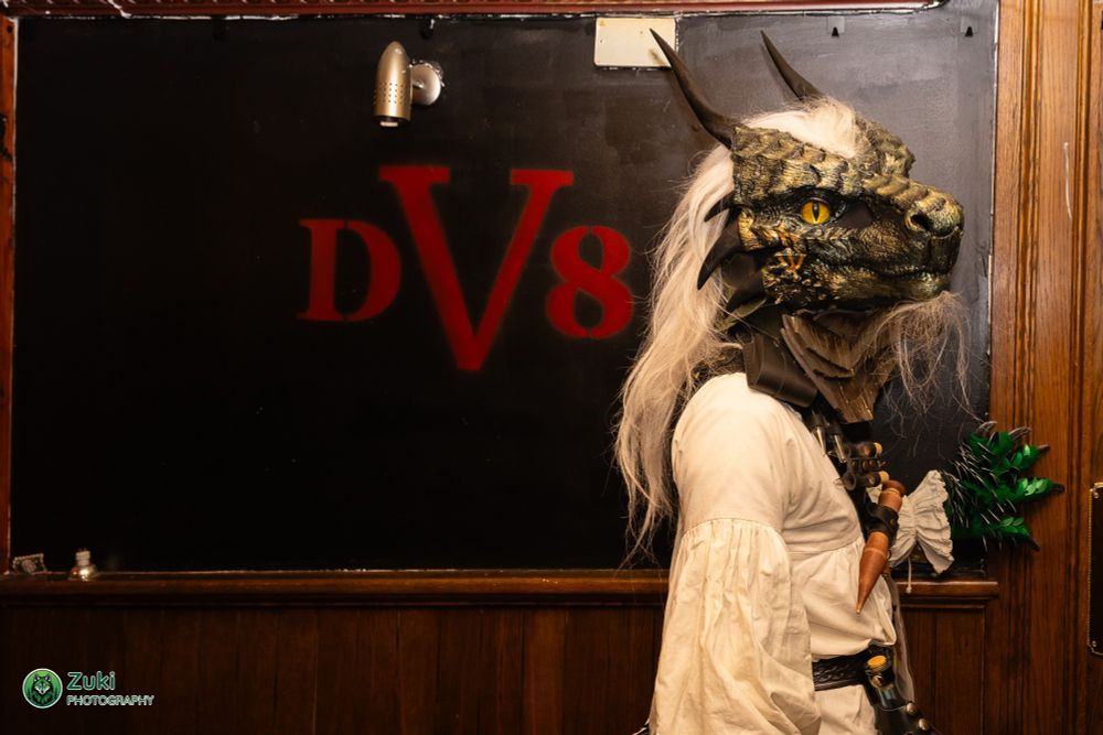 A suiter posing for a picture, with a sign in the background that says "DV8"