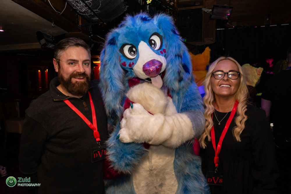 Two people posing for the camera either side of a large full fursuiter
