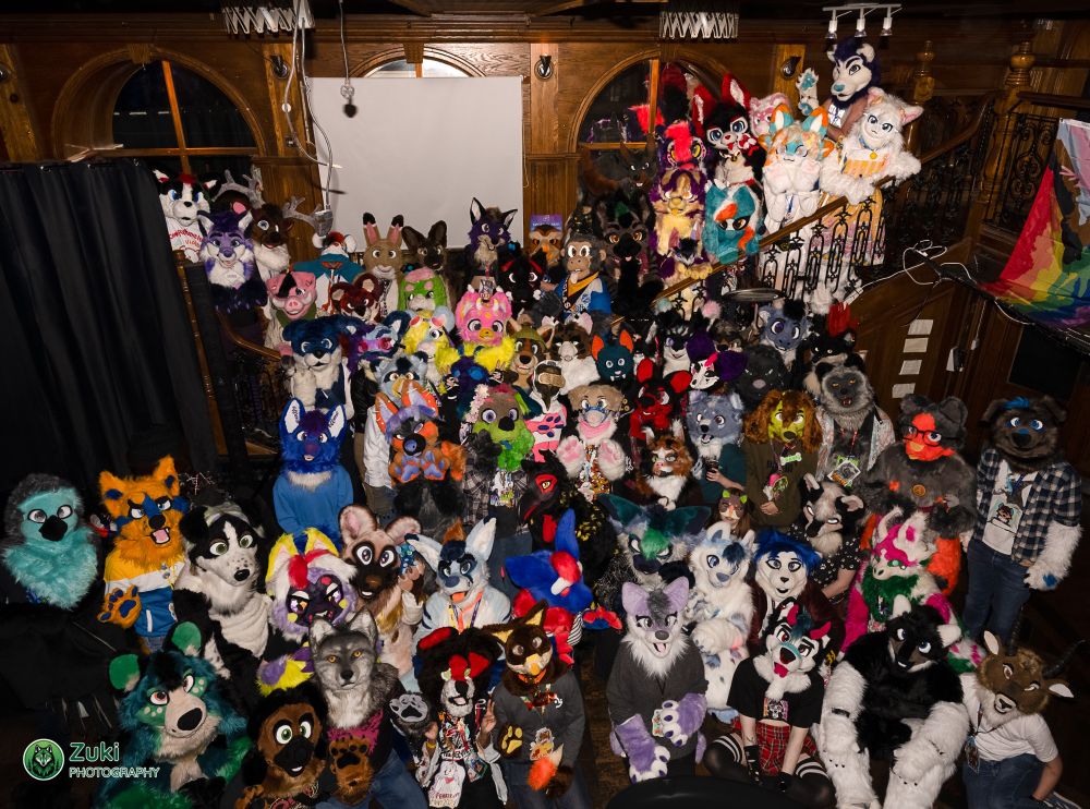 A large group of fursuiters posing for the camera, stacked up a staircase in a bar / club hall