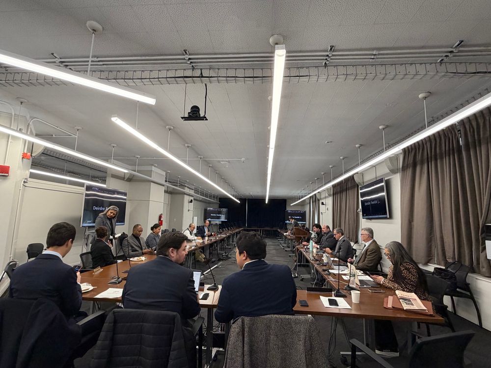 A large conference room with suits around a set of arranged tables, which is way larger than the number of people 