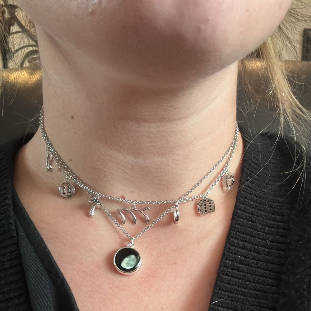 Selfie of the necklaces Iโm wearing, both Christmas presents! The longer is a circular, black pendant with a white gibbous moon in the center (it was the moon phase the day I was born), and the second necklace is a silver choker-style charm necklace with 7 small charms that all symbolize luck: a wishbone, a penny, a mushroom, a 777, a horseshoe, a rolling die, and a 4 leaf clover.