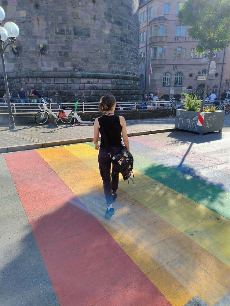 Ein in schwarz gekleidetes WasdNedSagsd geht über den Regenbogenstreifen unweit des Nürnberger Hauptbahnhofs.
