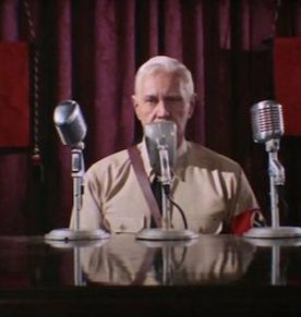 John Gill, the Führer of the planet Ekos in Star Trek episode 'Patterns of Force,' sits behind several microphones with one obscuring his mouth.