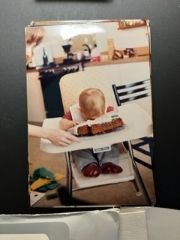 An old family photo of a child in a high chair planting their face into their birthday cake.