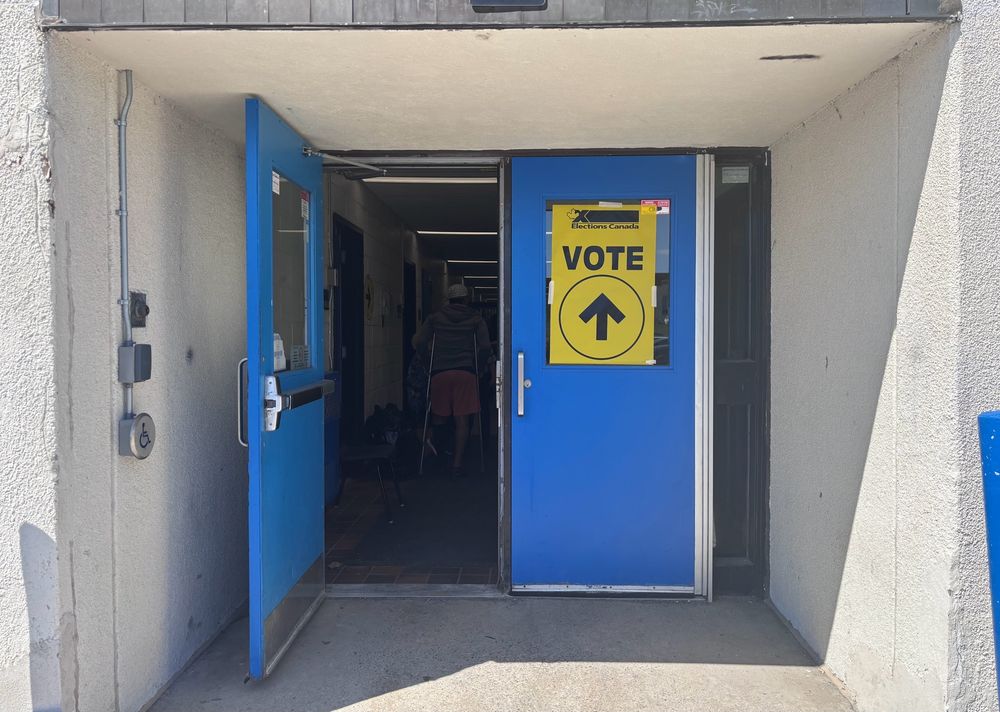 Portes bleues à double battant, l'une est ouverte, l'autre porte un panneau VOTE jaune, au-dessus d'une flèche noire.