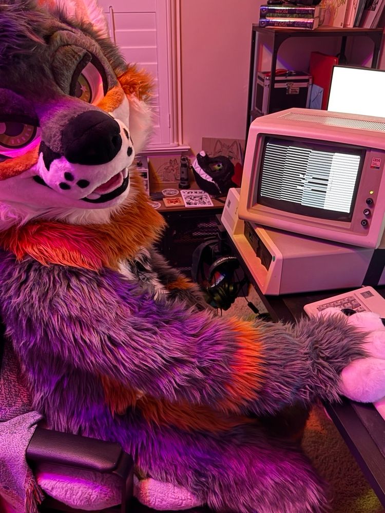 Me in fursuit sitting at my desk where my IBM XT is displaying the cover page of a Telnet literary magazine!