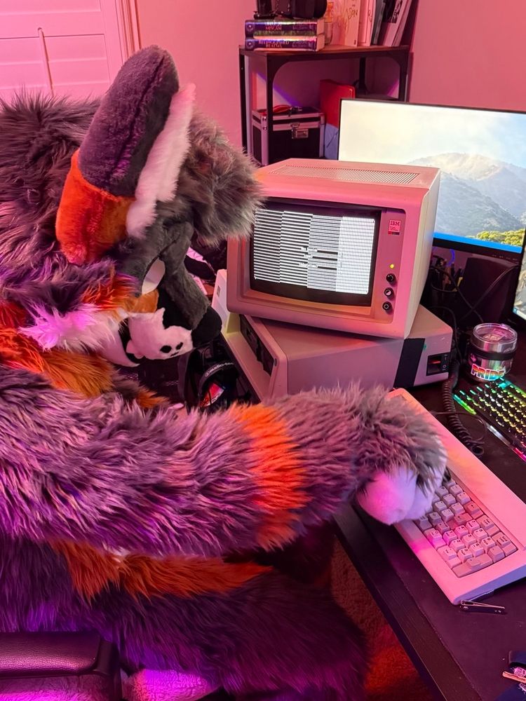 Me in fursuit sitting at my desk where my IBM XT is displaying the cover page of a Telnet literary magazine!