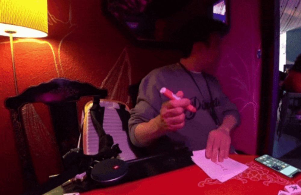 a man sitting at a table with a marker in his hand and a shirt that says ' dirty ' on it