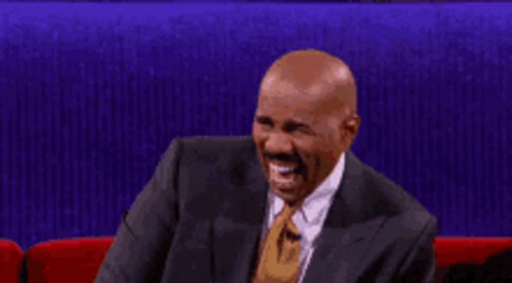 a man in a suit and tie is laughing while sitting on a red couch .