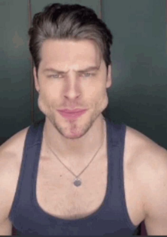 a man wearing a tank top and a necklace is making a face .