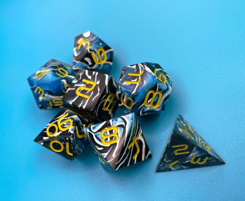 A 7 piece dnd set on a blue background. The dice are swirled with blue, black and white, with gold yellow numbers.