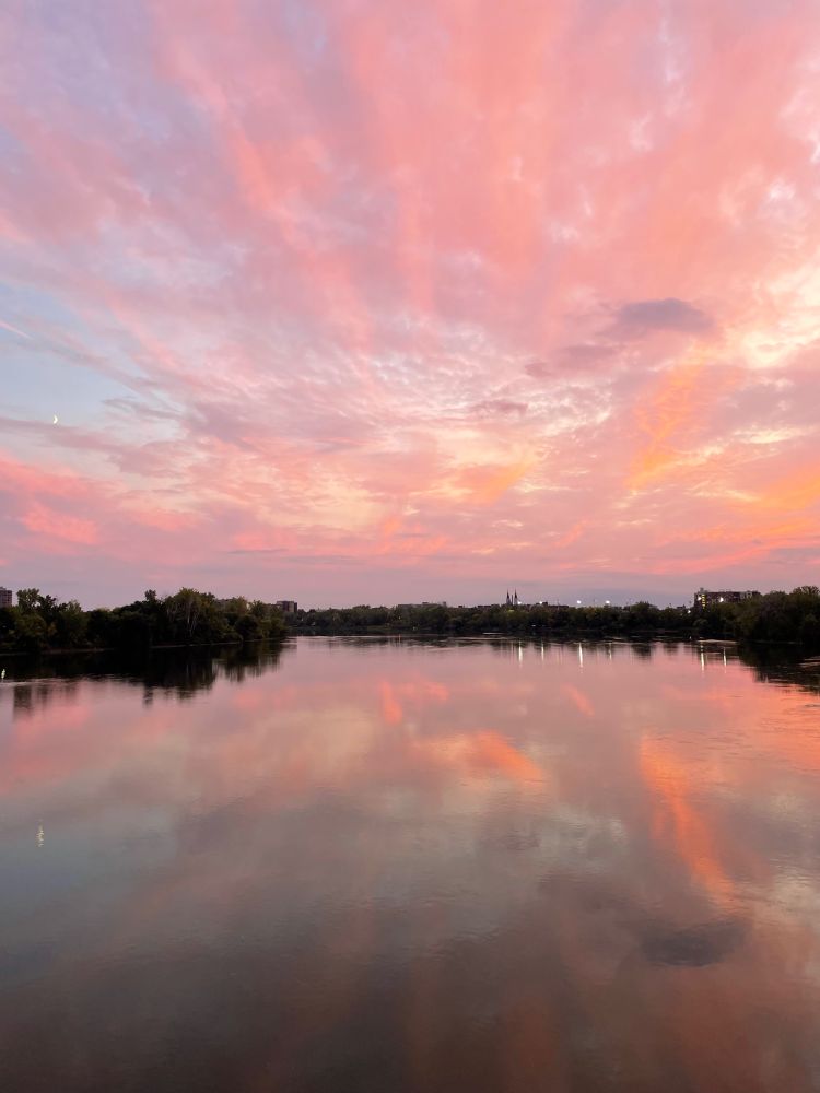 Picture of pink and orange clouds at sunset, reflected in the calm river water below.