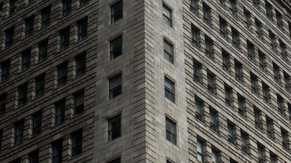 Color digital photo of a dull grey brown brick building in Chicago at a 45° angle at the corner. One side is bathed softly in warm sunlight and the other in slowly deepening shadows