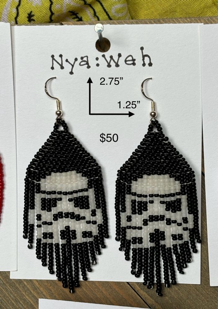 A pair of black fringed earrings with white Stormtrooper helmets displayed on a card with Nya:weh at the top and a label showing 2.75" tall and 1.25" wide for $50.