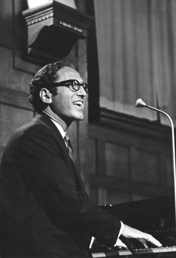 Lehrer playing piano in thick glasses, black and white photo.