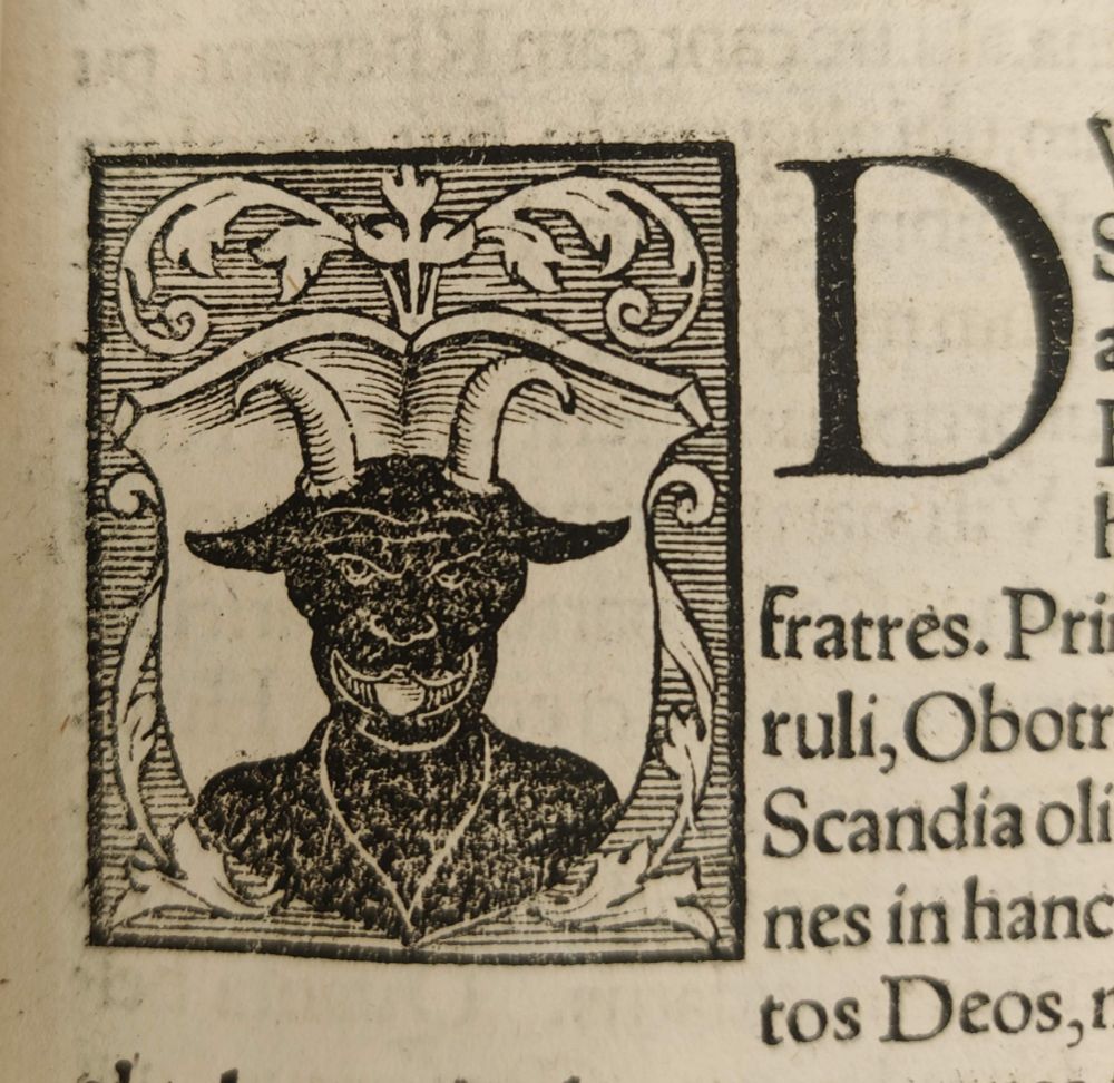 Black goat in a shield woodcut, upright and grinning at you. Big initial D on the right.