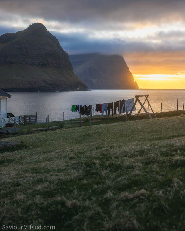 Clothes hanging outside the house with a view of the ocean and cliffs at sunset. The place is Viðareiði, Faroe Islands