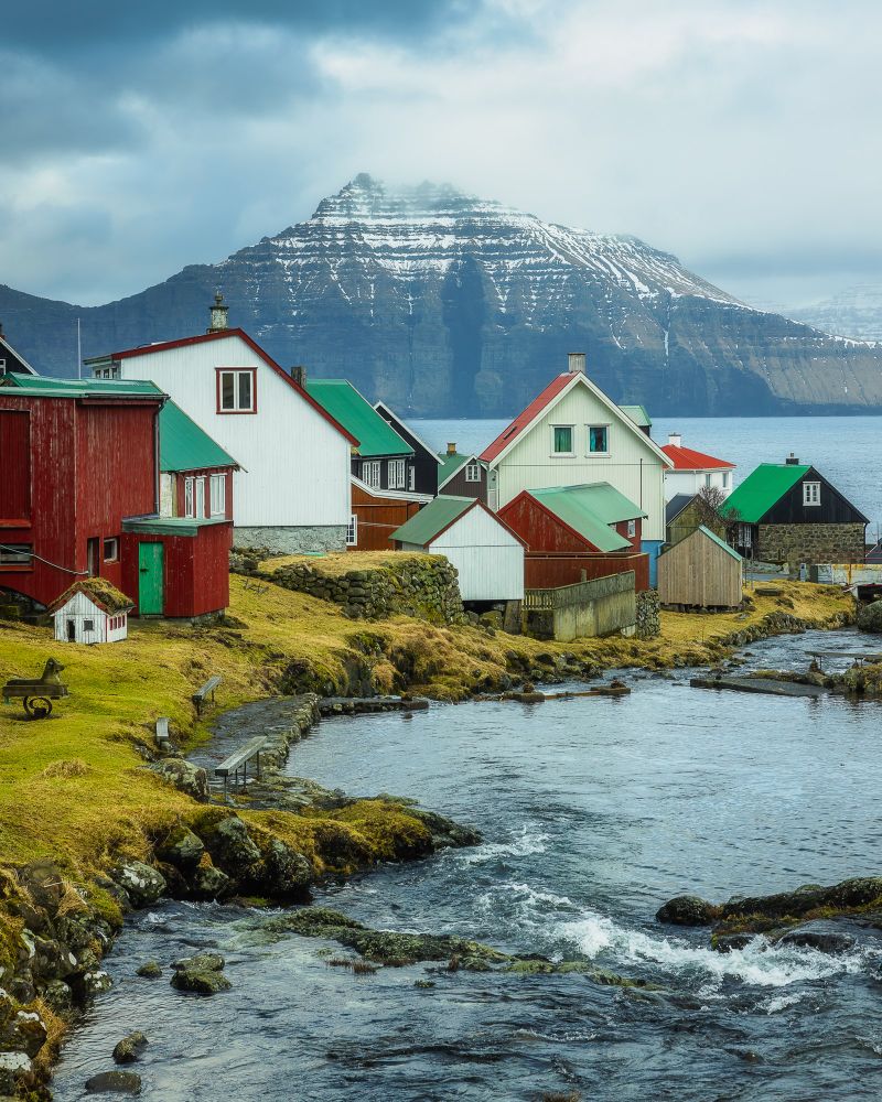 River, nordic houses and the background of Kalsoy with the mountain peaks covered in snow.