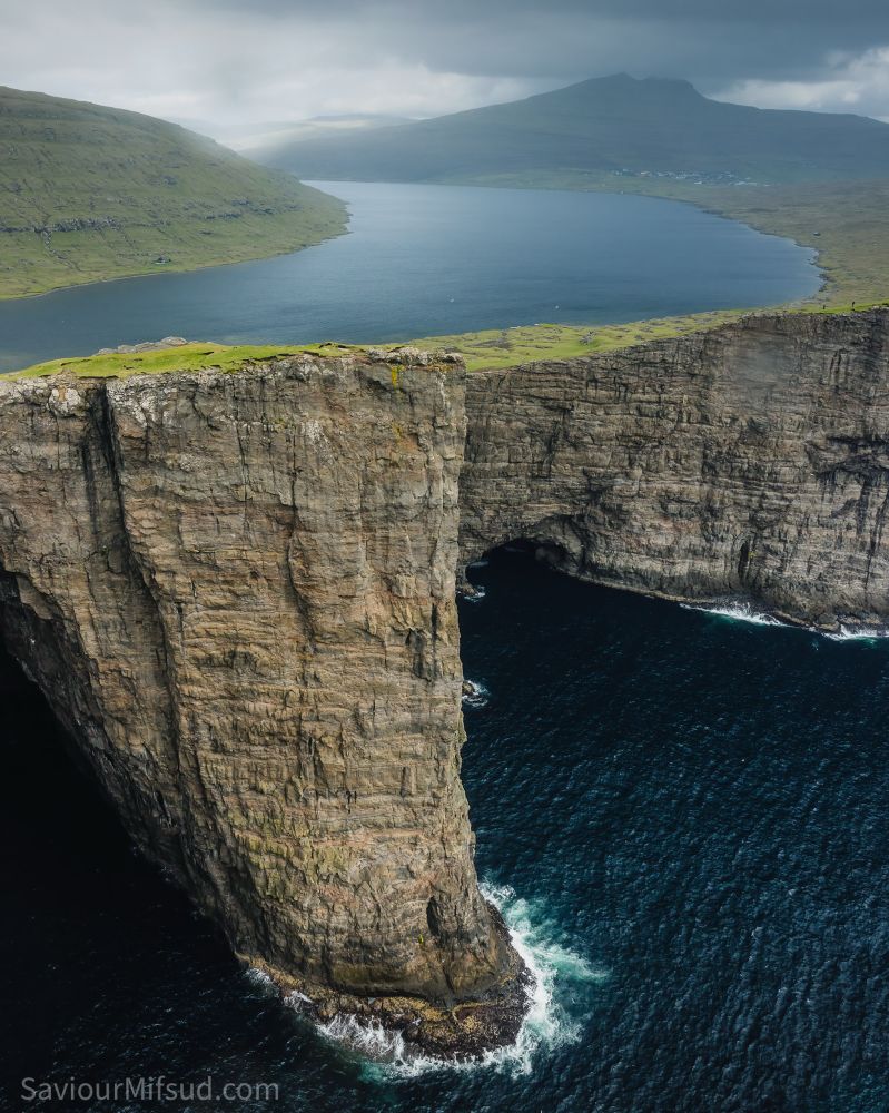Trælanípa, Faroe Islands also called the lake above the ocean. Atlantic Ocean, high cliffs, and a lake surrounded by green grass and a village in the background.