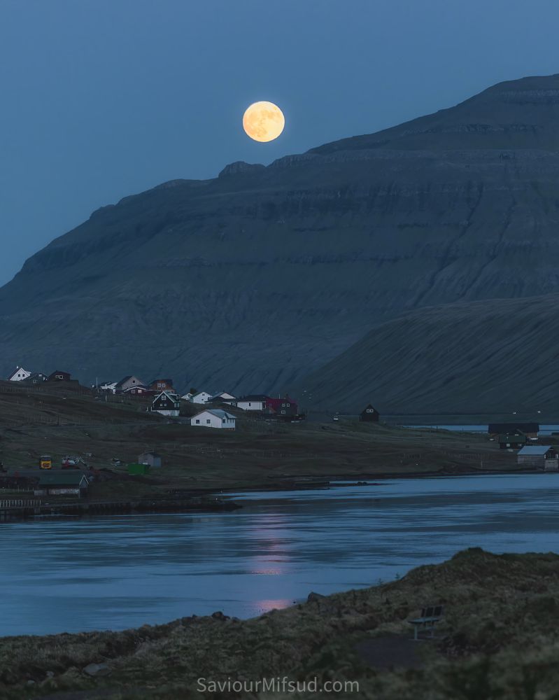 Moonrise from behind the mountain at the village of Oyrabakka, Faroe Islands. Reflection in the water of the moon light.